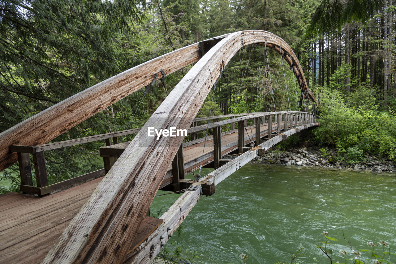 Modern arched footpath suspension bridge over river in rainforest.