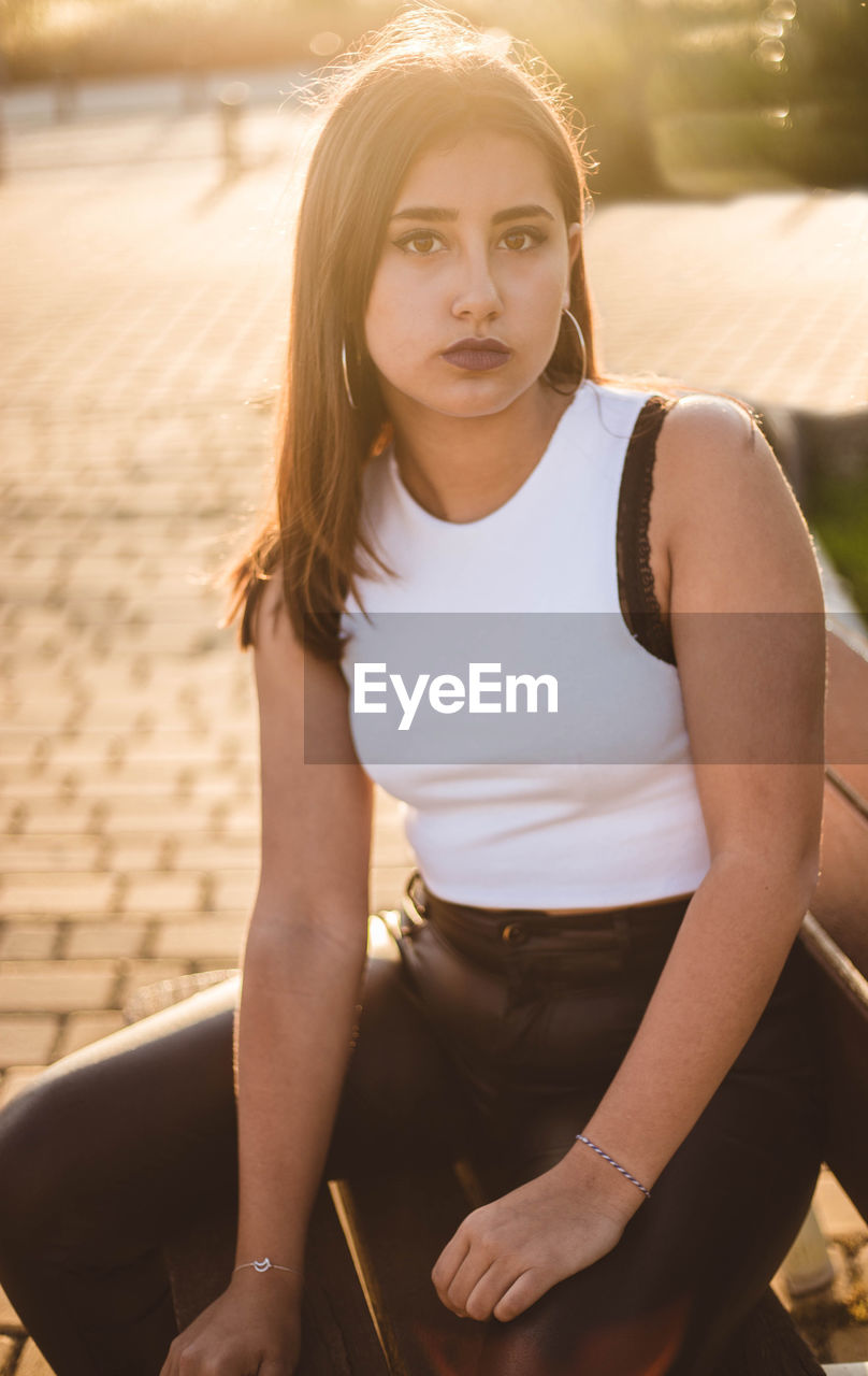 Serious teenager with a intense gaze sitting on a bench at sunset