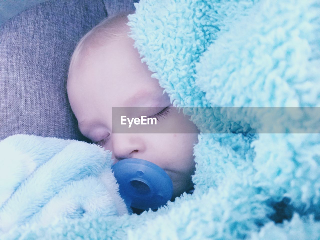 Close-up of baby boy sucking pacifier while sleeping on bed