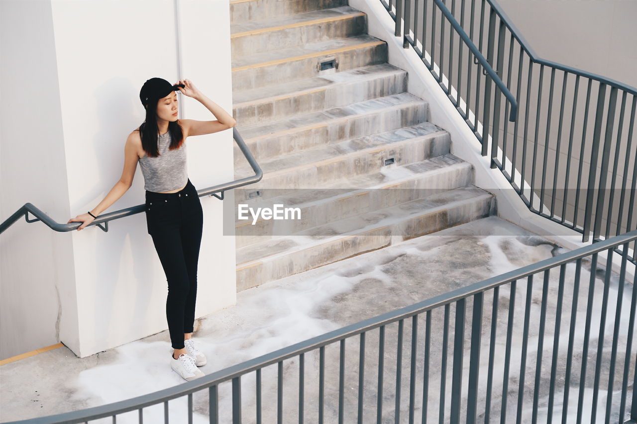 Full length of young woman standing by railing on staircase