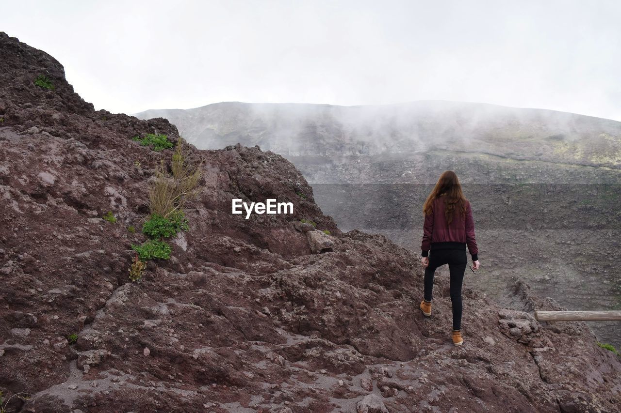 Rear view of woman standing on mountain against sky