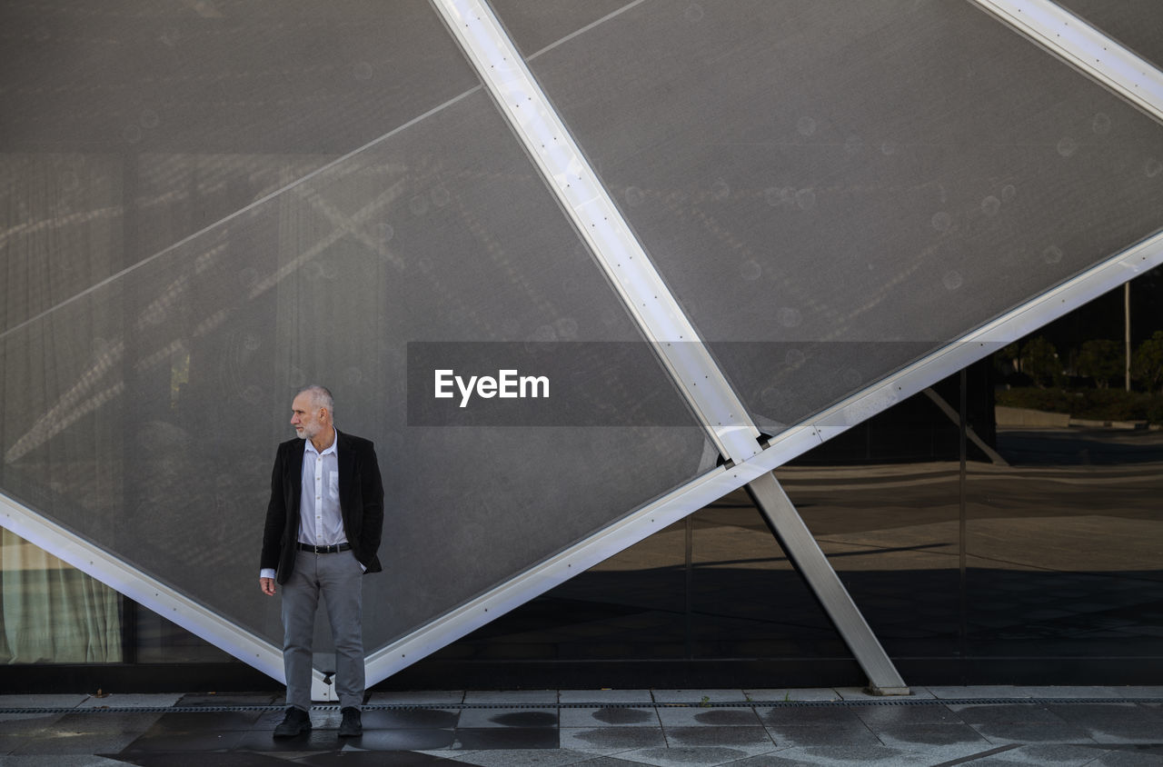 Portrait of adult man in suit against glass wall in business district