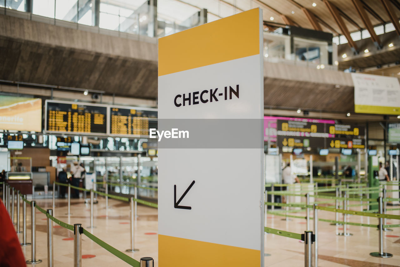 White check in direction board near counters with metal pillars in modern light public airport with flight schedule on contemporary signboards