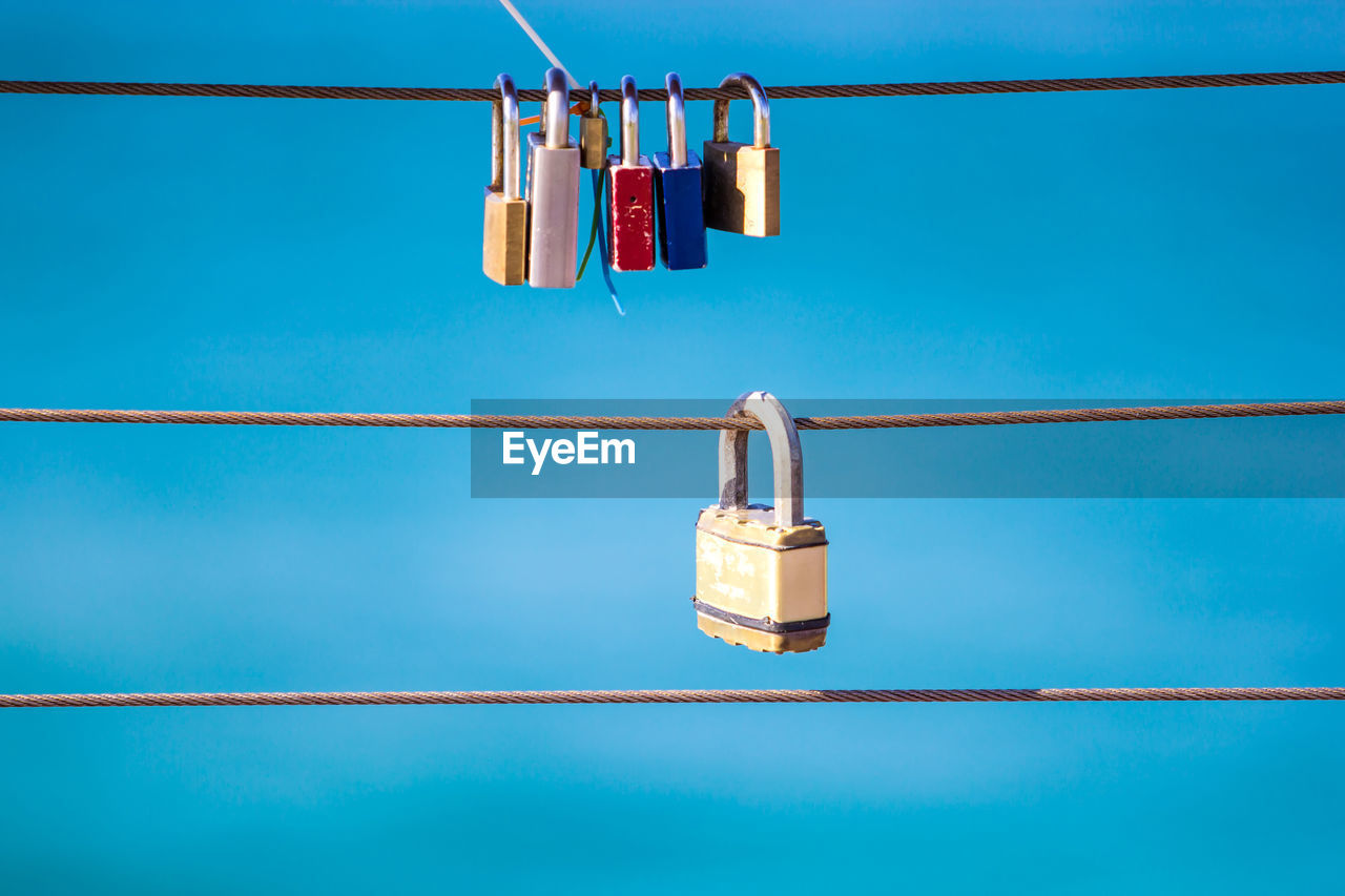 Low angle view of padlocks on steel cable against blue sky