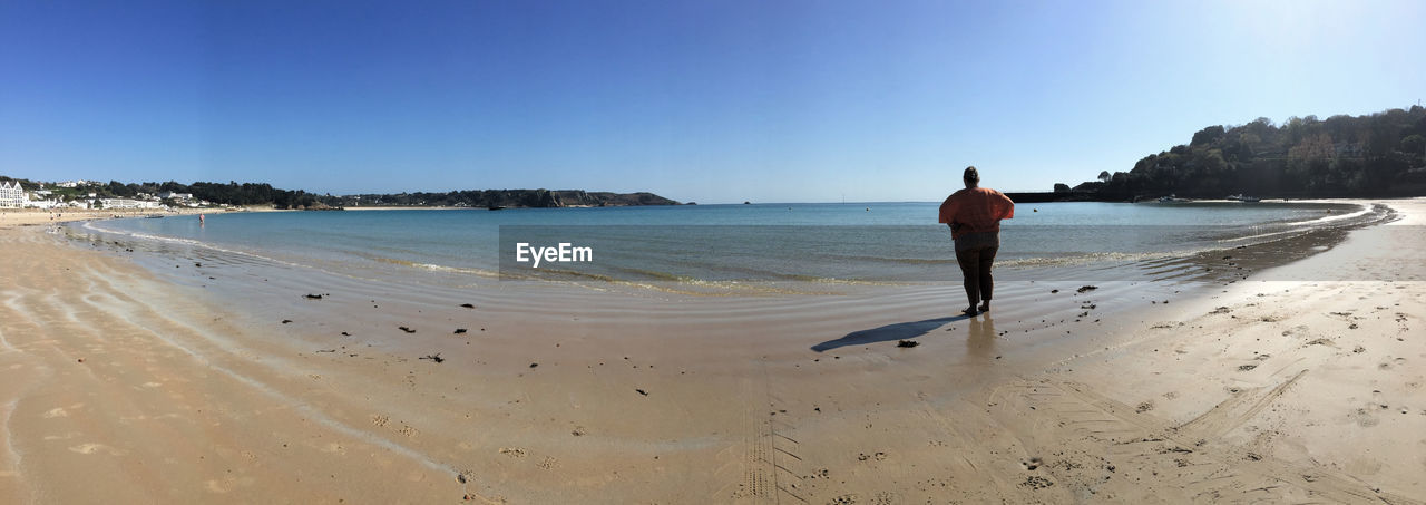 Full length rear view of person standing at beach against sky on sunny day