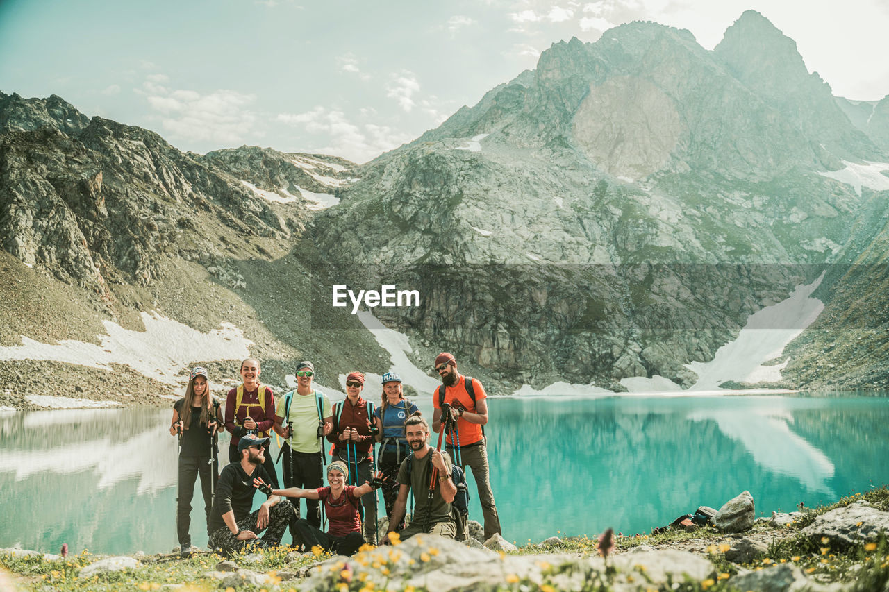 PEOPLE STANDING ON MOUNTAIN BY LAKE AGAINST SKY