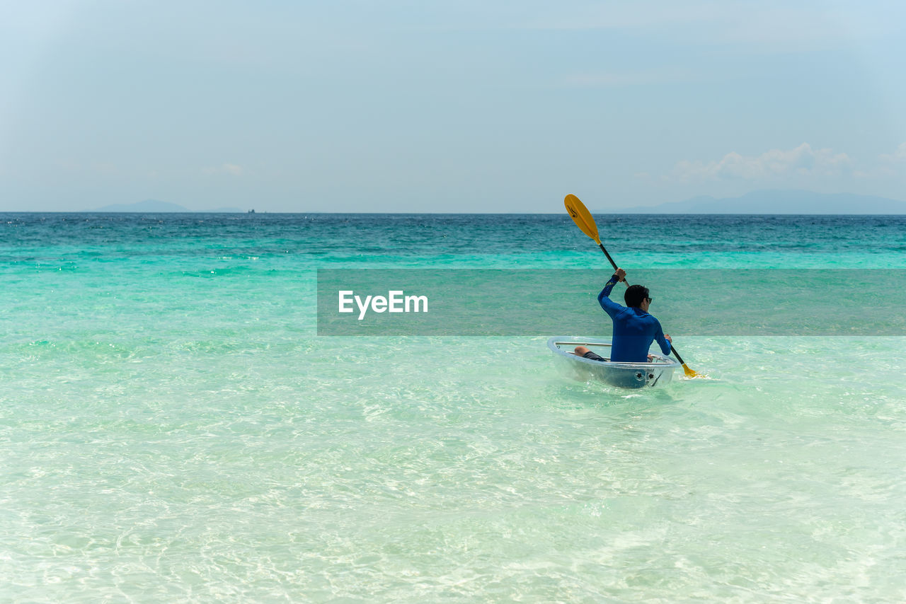 Rear view of asian male who is kayaking close to beach.