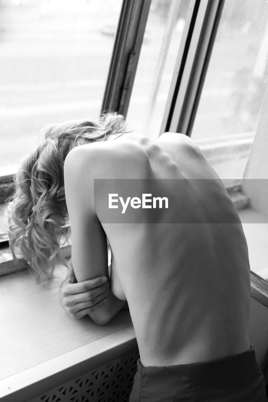 High angle view of topless young woman standing by window at home