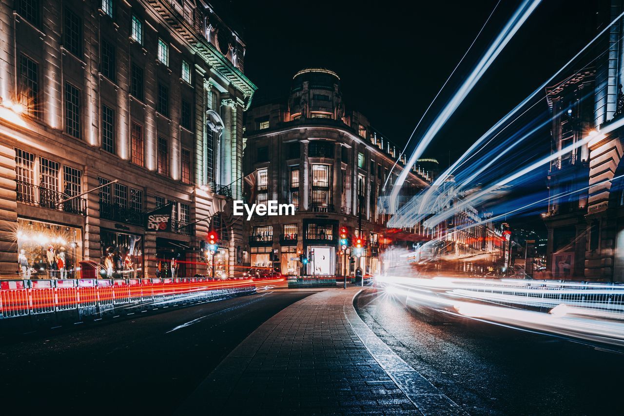 Illuminated city street and buildings at night with light trails