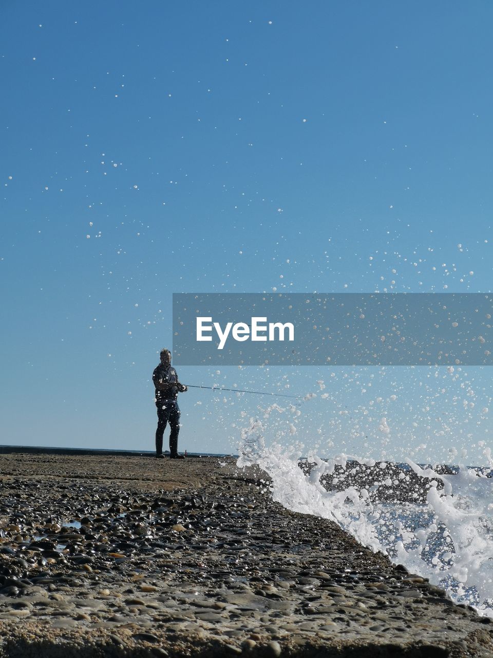 Full length of man fishing in sea while standing against clear sky