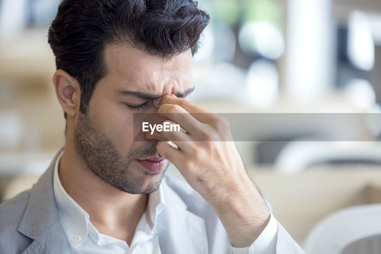 A tired young man's eyes are tired from computer work, while a stressed man suffers from a headache