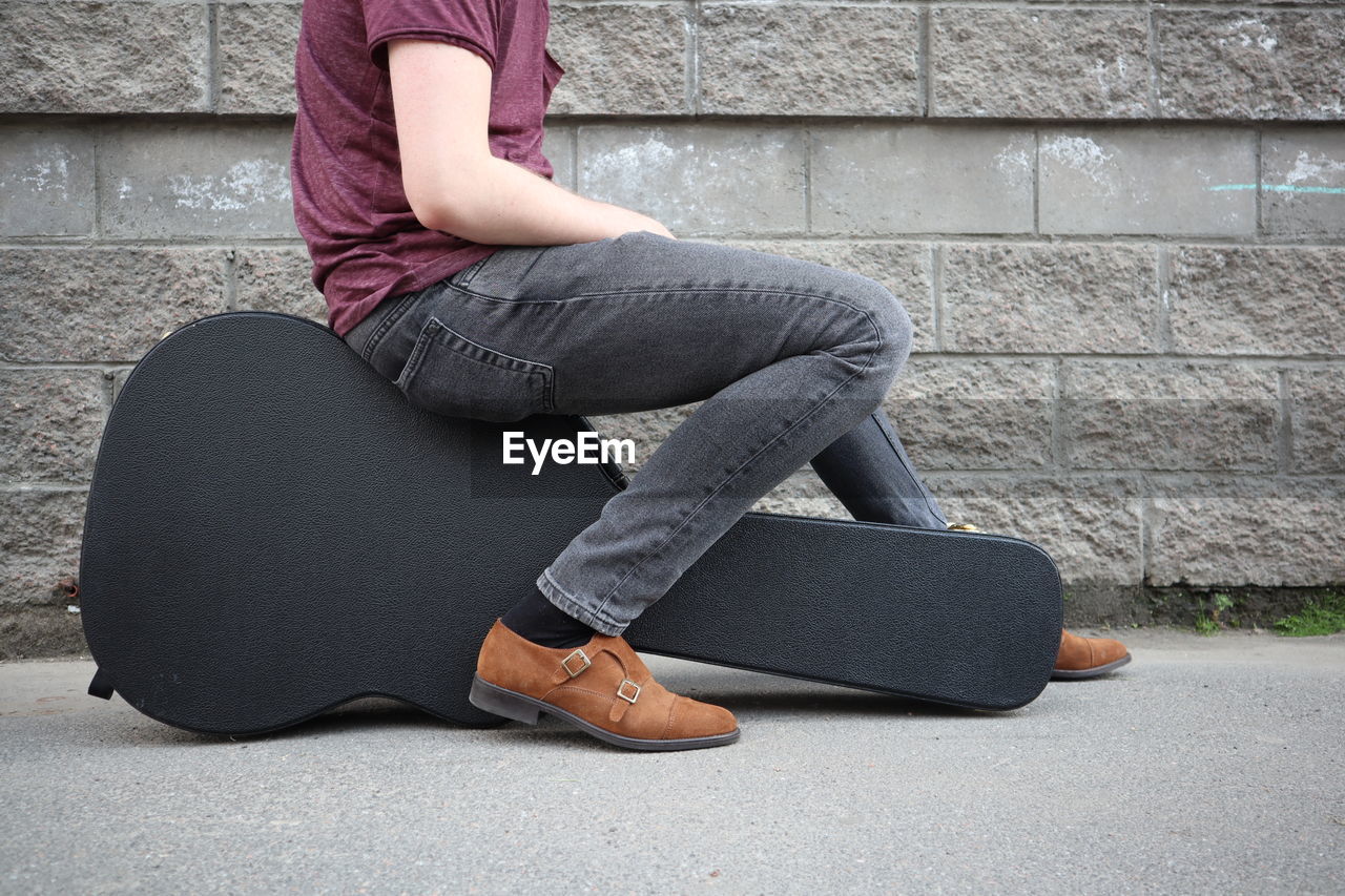 LOW SECTION OF WOMAN SITTING ON FLOOR AGAINST WALL