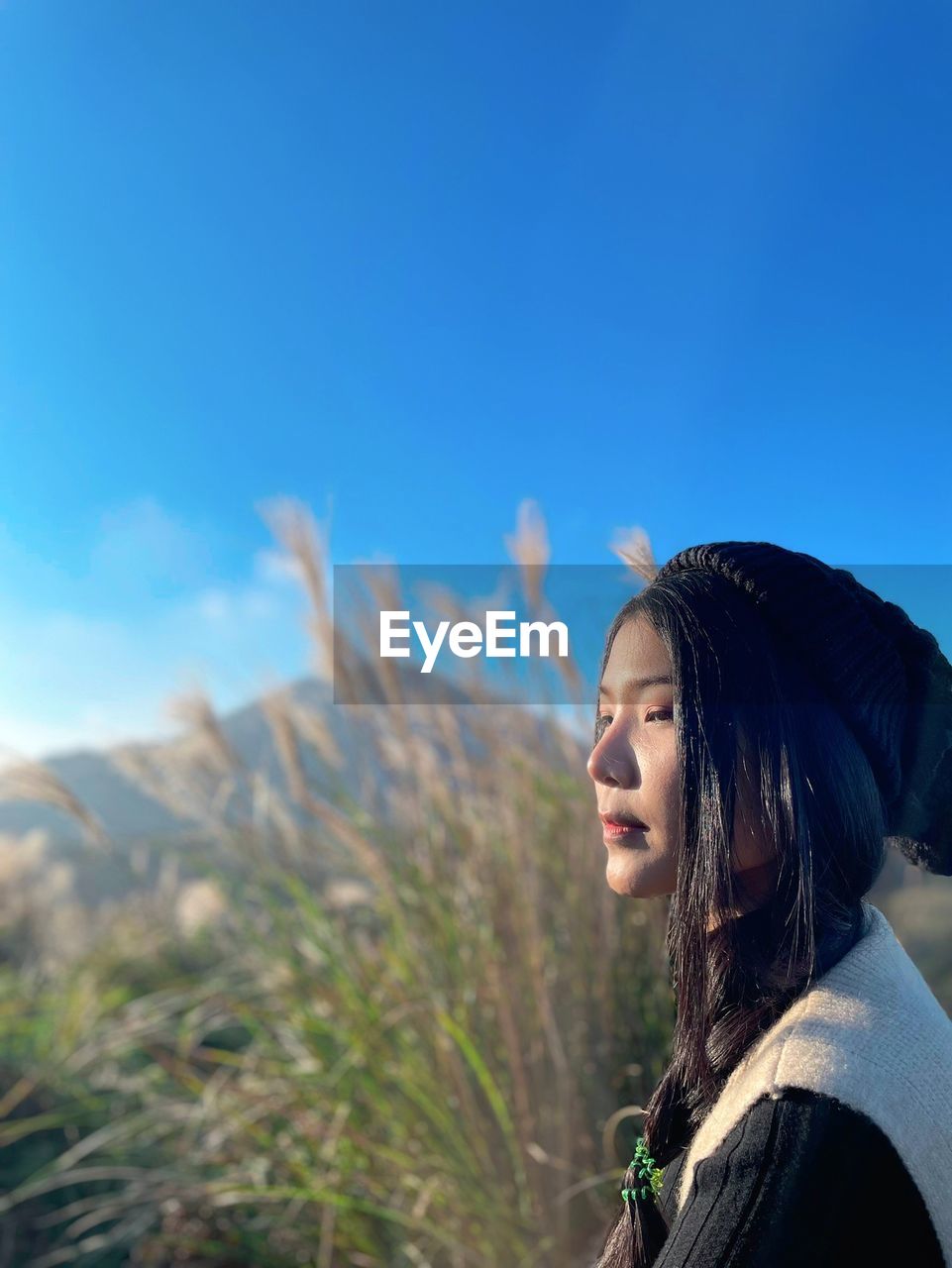 side view of young woman looking away against clear blue sky