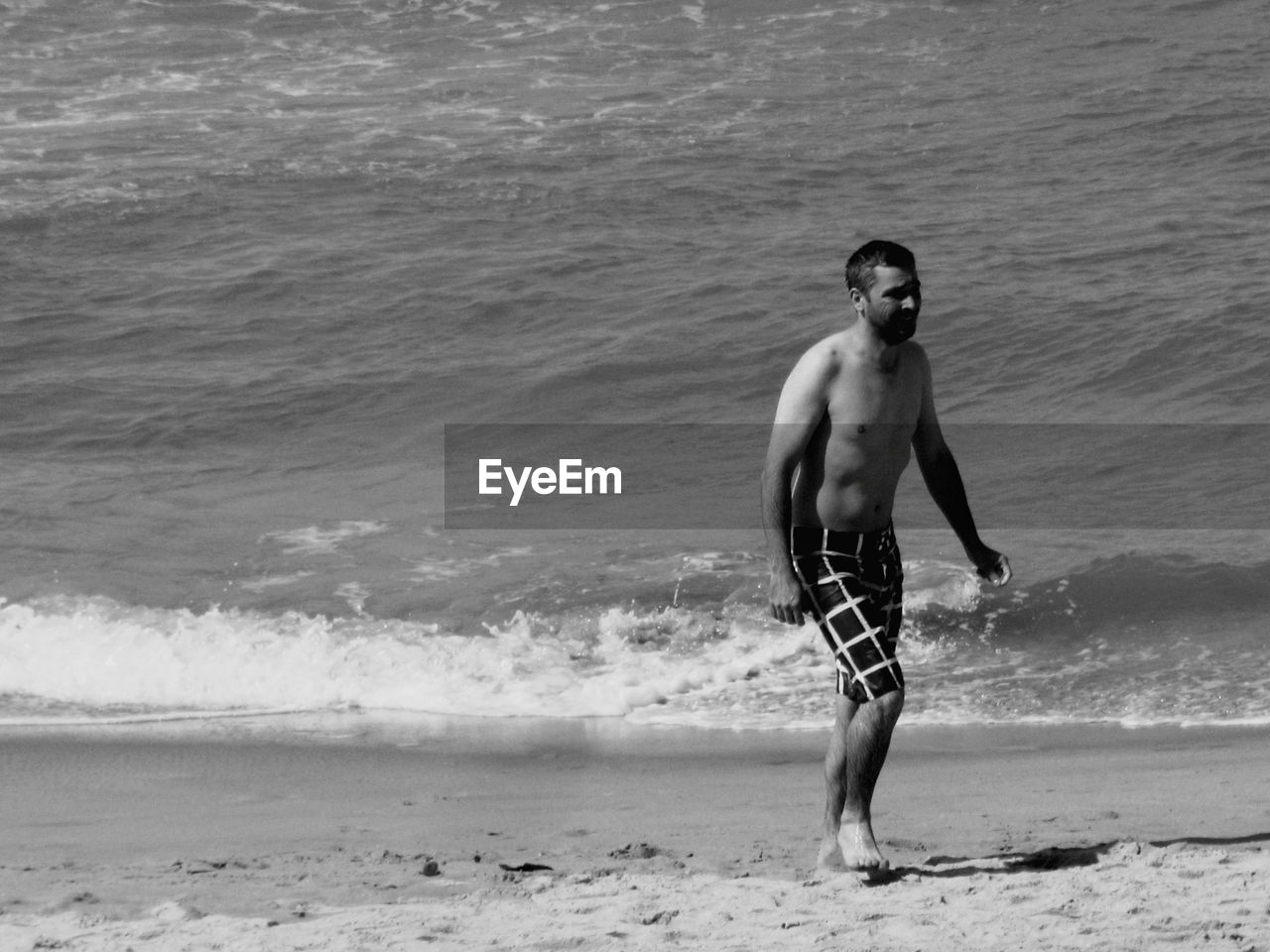 Shirtless man walking on shore at beach