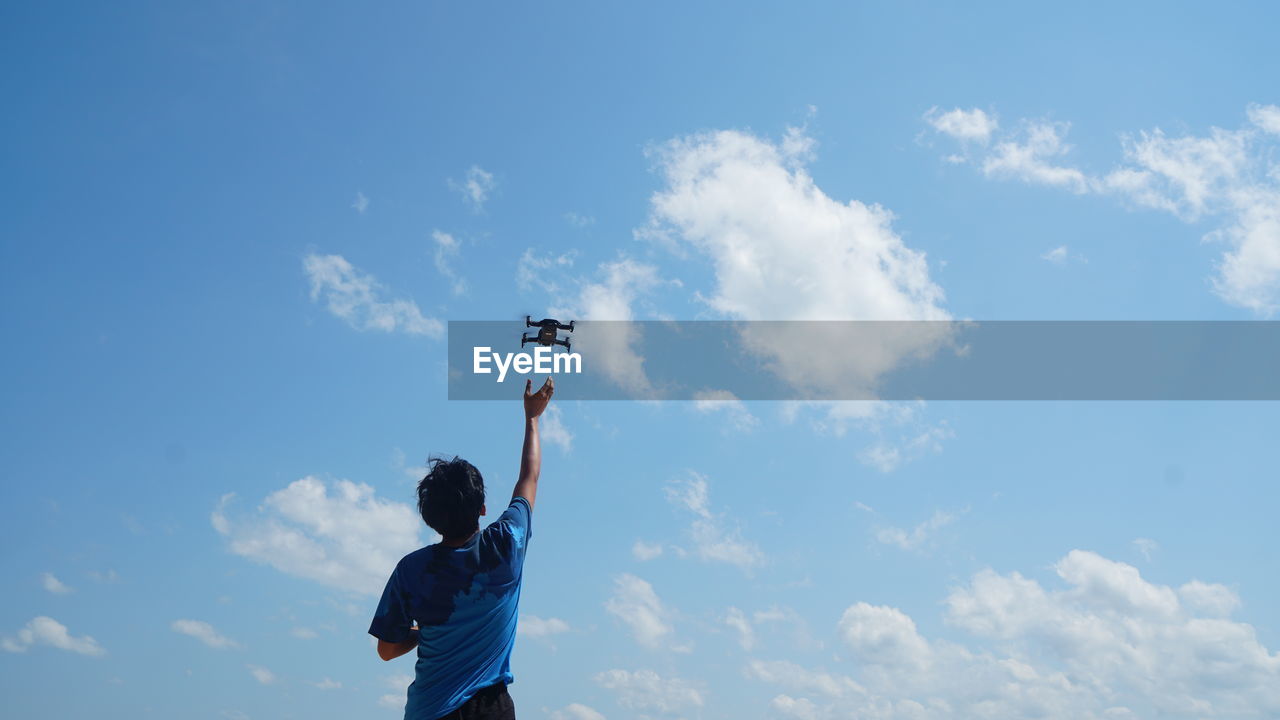 Low angle view of man flying drone against sky