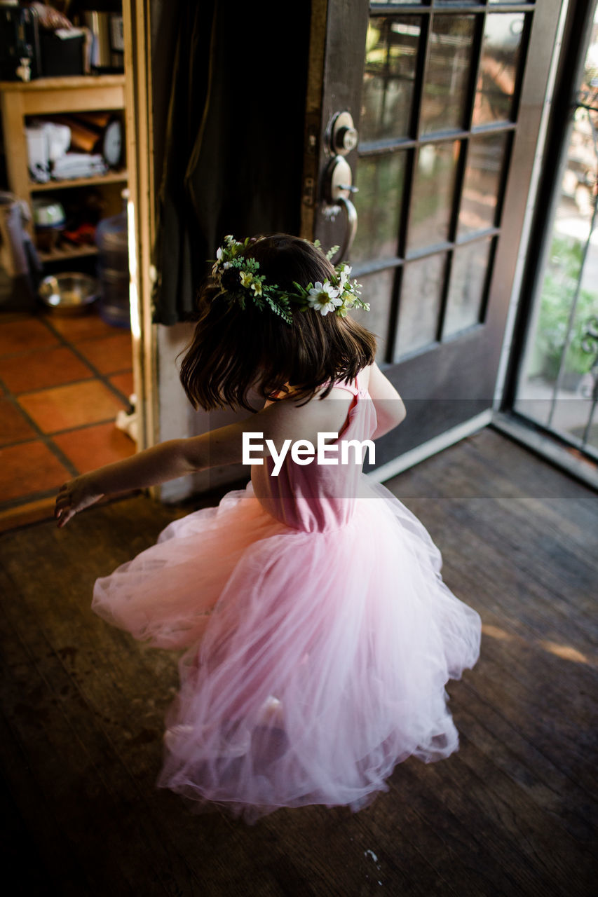 Young girl spinning by front door wearing tutu and flower crown