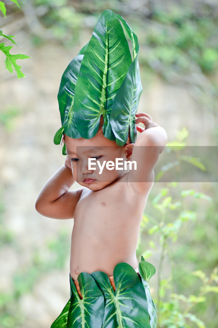 Cute boy wearing leaves and garland standing outdoors