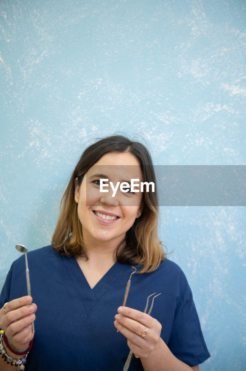 Portrait of smiling dentist holding medical equipment against wall