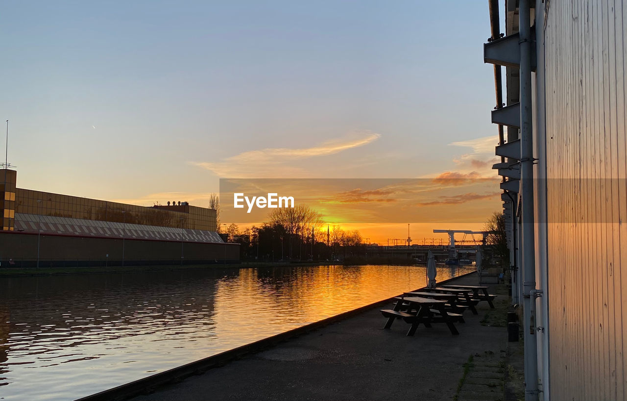 VIEW OF RIVER BY BUILDINGS AGAINST SKY DURING SUNSET