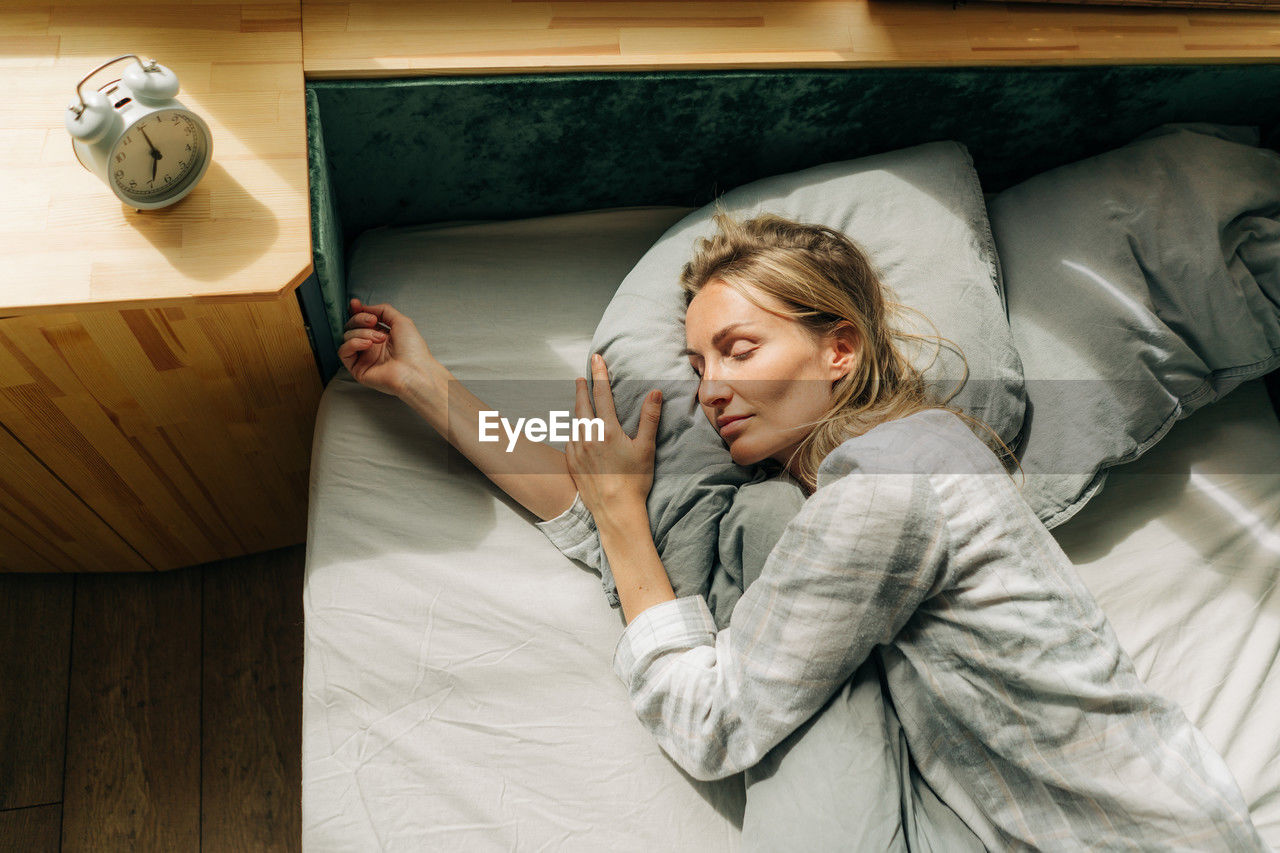 Lifestyle portrait of a woman in pajamas sleeping while lying in bed blissfully.