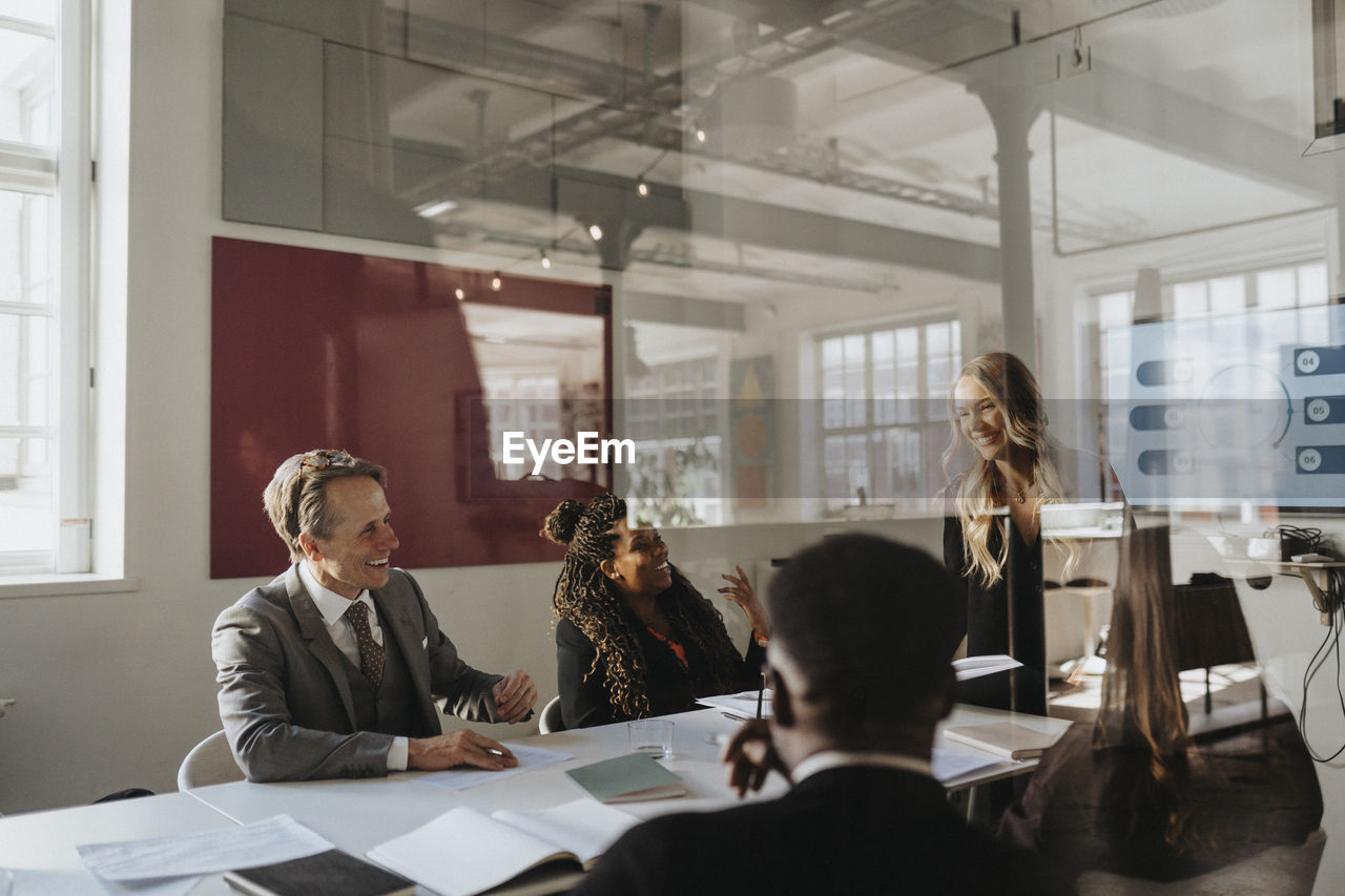 Happy male and female entrepreneurs during business meeting at office seen through glass