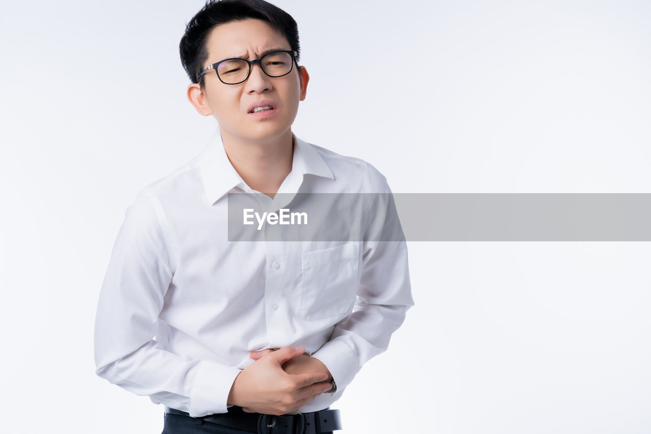 PORTRAIT OF YOUNG MAN STANDING AGAINST GRAY BACKGROUND