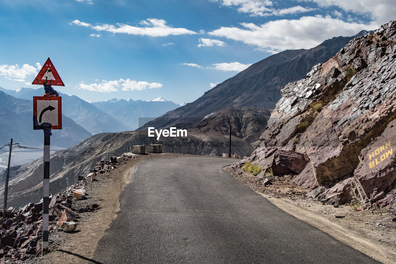 Road by rocky mountains against cloudy sky