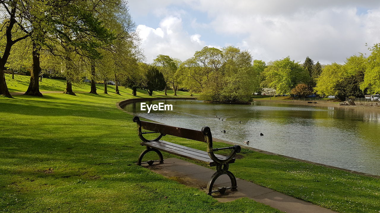 Empty bench in park by lake against sky