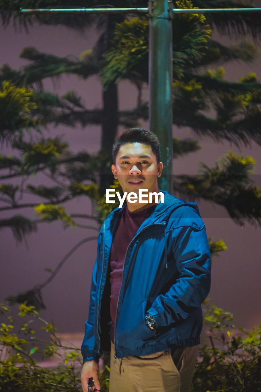 Portrait of young man standing against trees at night