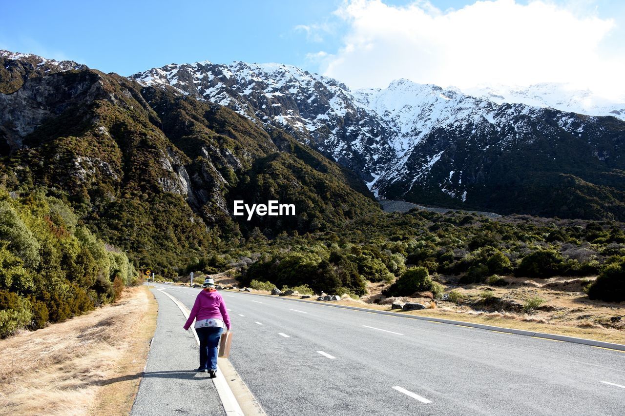 Rear view of woman walking on road leading toward mountain