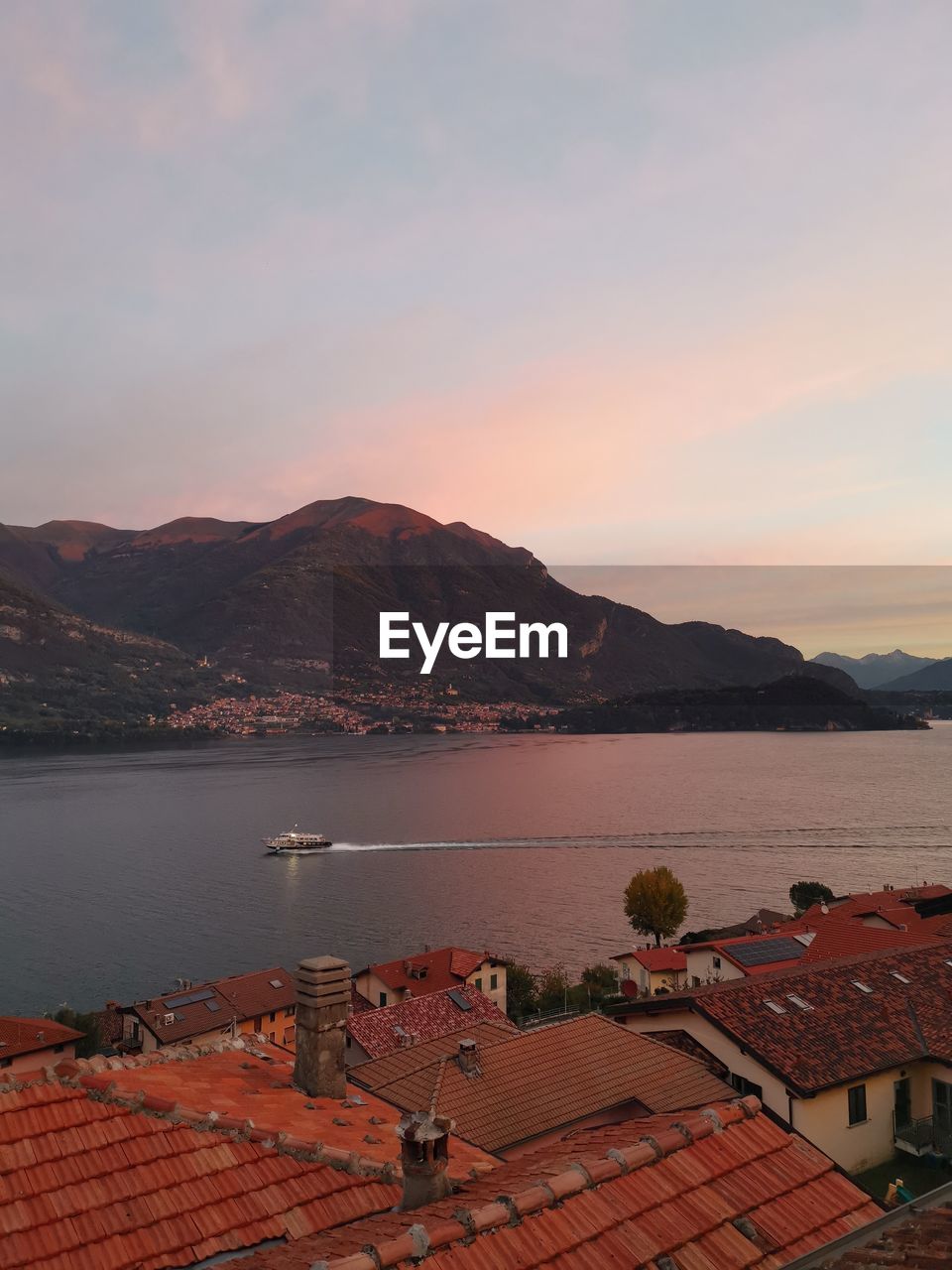 Early morning ferry on the lake at sunrise with view over terracotta rooftops on lake como in italy