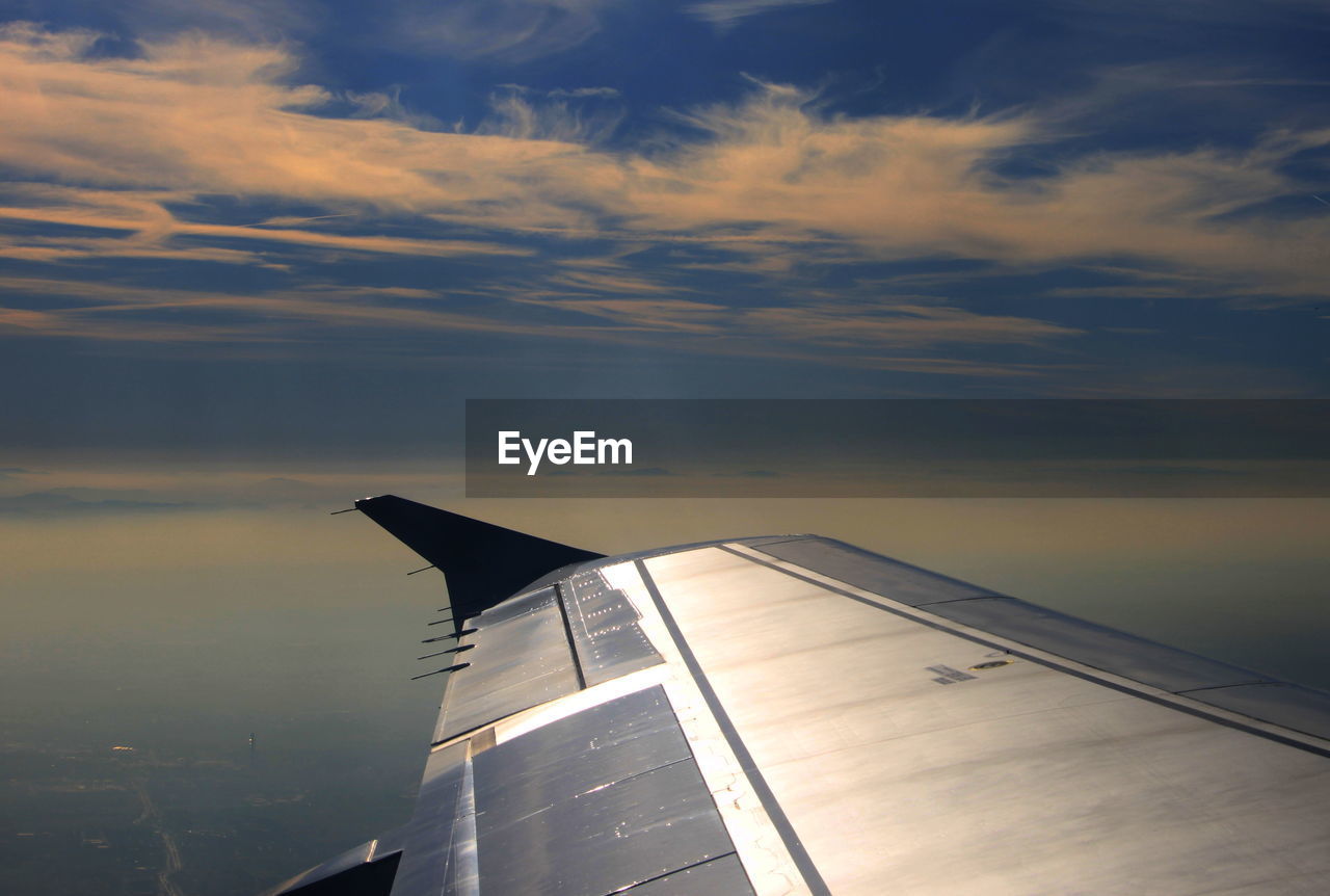 CLOSE-UP OF AIRPLANE WING AGAINST SKY AT SUNSET