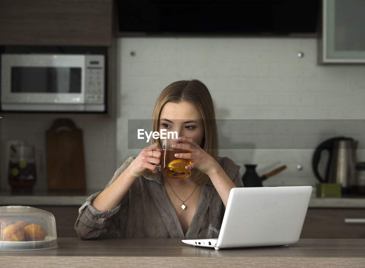 Woman drinking tea while using laptop