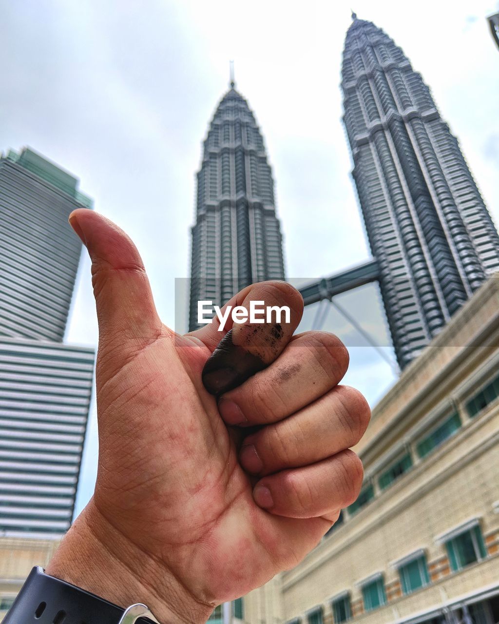 LOW ANGLE VIEW OF CROPPED HAND AGAINST BUILDINGS IN CITY