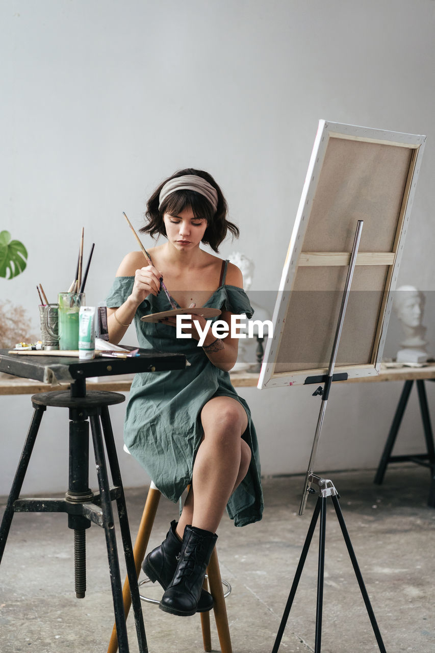 Young woman painting on canvas while sitting on table