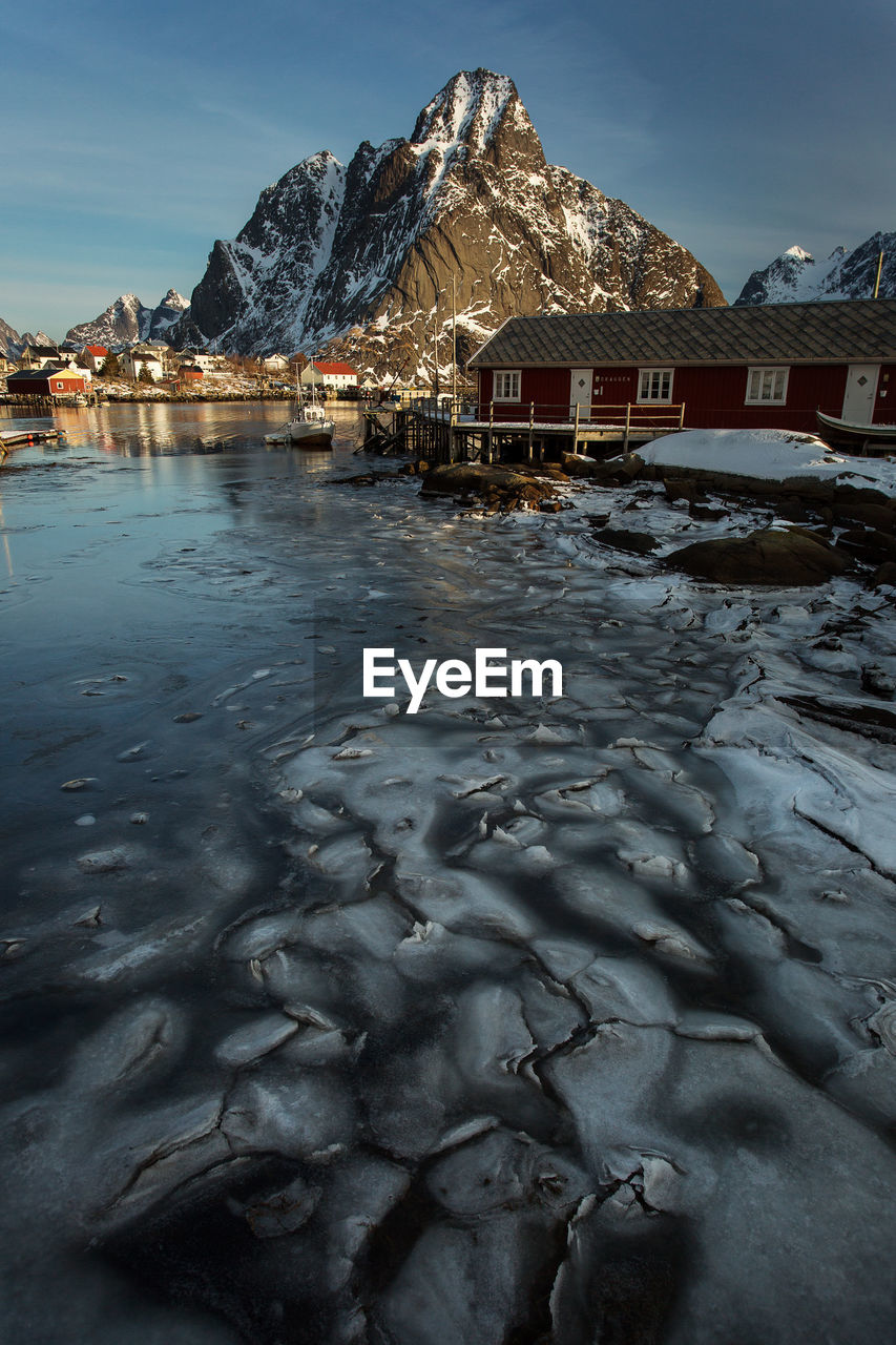 Scenic view of frozen lake by houses against sky during winter