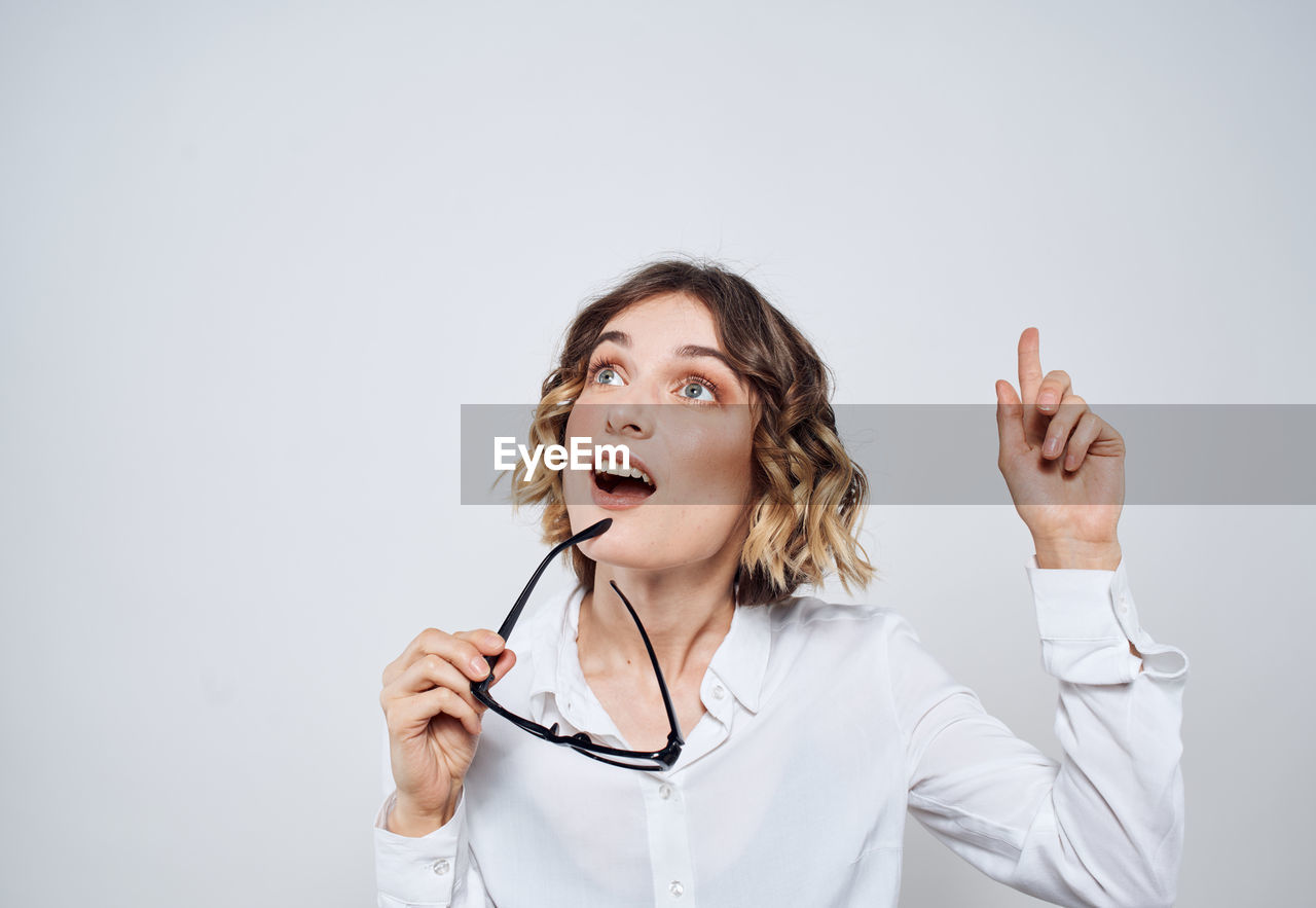 one person, adult, women, studio shot, person, indoors, portrait, mouth open, emotion, finger, gesturing, female, human mouth, human face, young adult, copy space, clothing, waist up, hand, communication, listening, arm, facial expression, positive emotion, occupation, singing, front view, business, happiness, hand raised, white background, looking, shouting, businesswoman, music, microphone, fun, looking up, white, arms raised, hairstyle