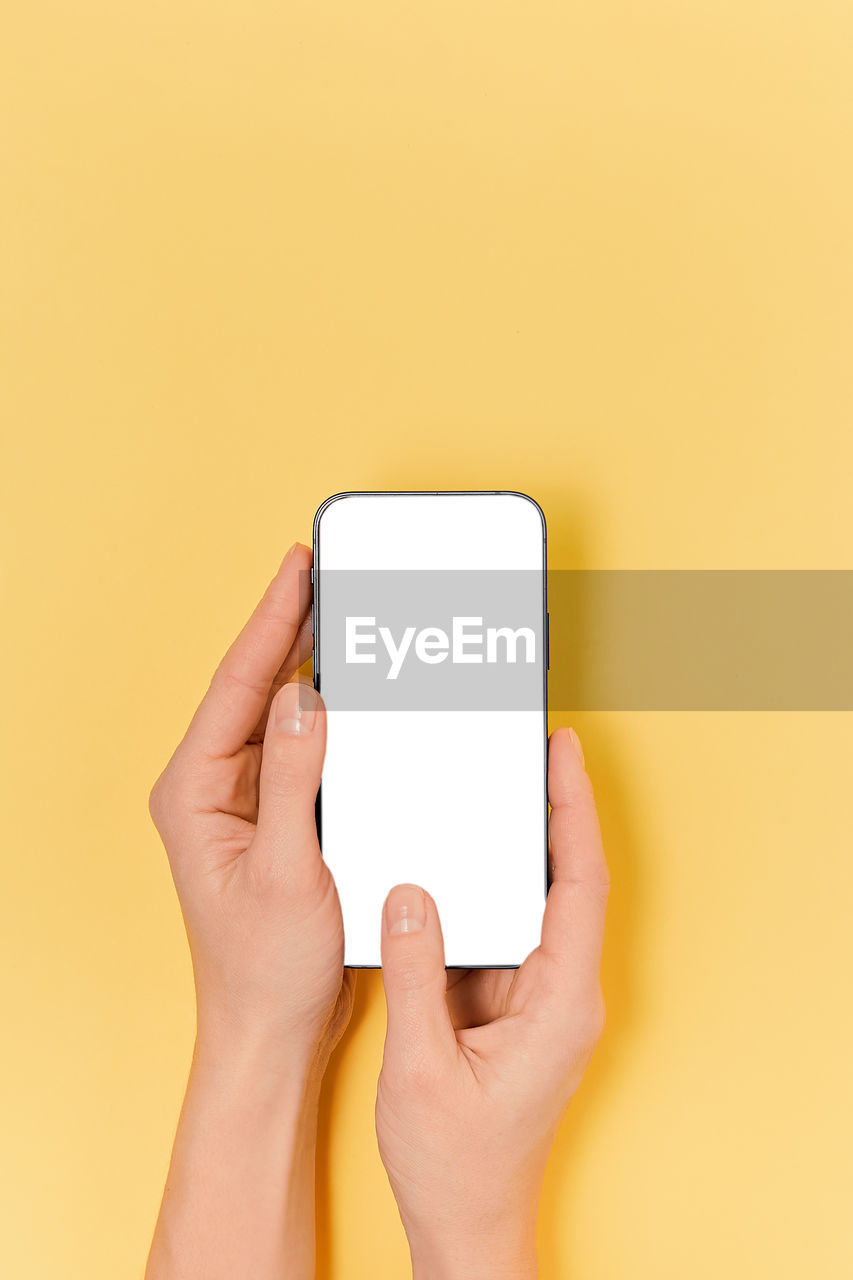 cropped hands of woman using mobile phone against yellow background