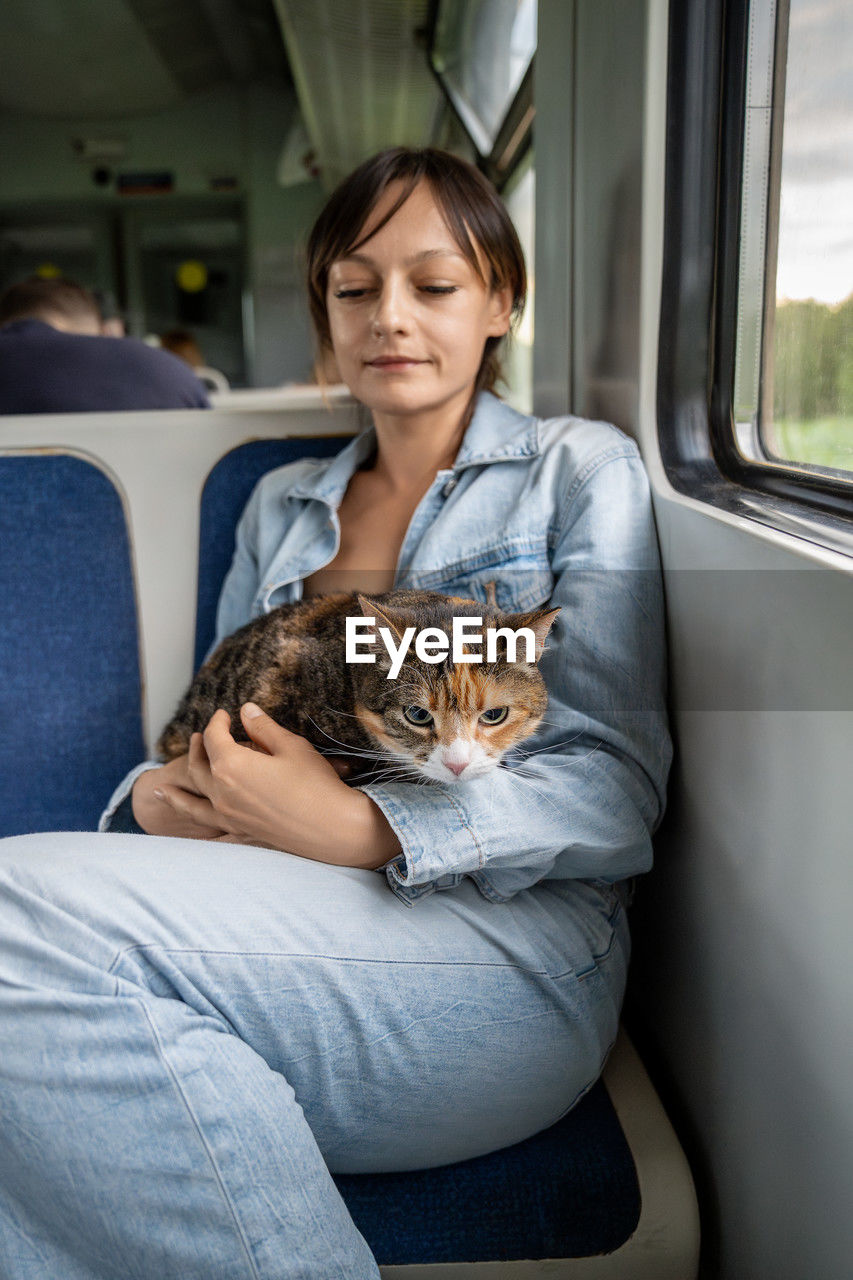 Pensive woman hugging cuddling with cat traveling in train. stressed kitty sitting on laps of female