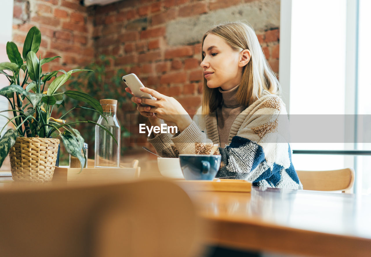 Young woman using smart phone while sitting on table