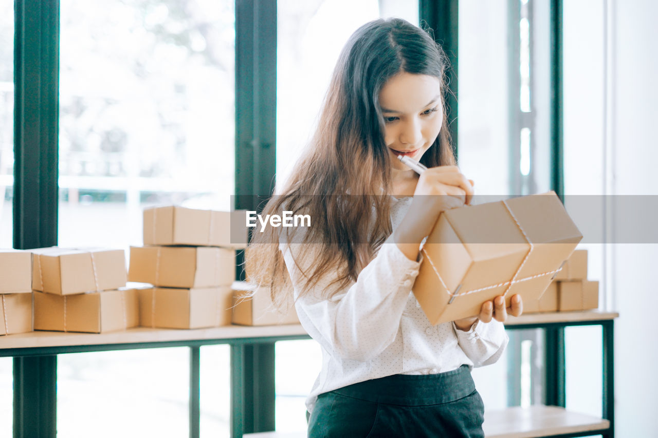 Young businesswoman writing on package at office