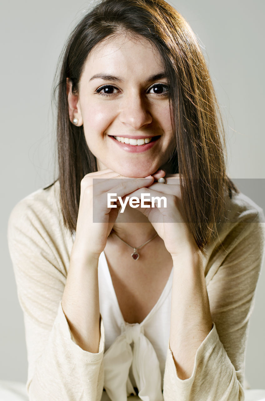 Portrait of smiling young woman leaning on elbows against gray background