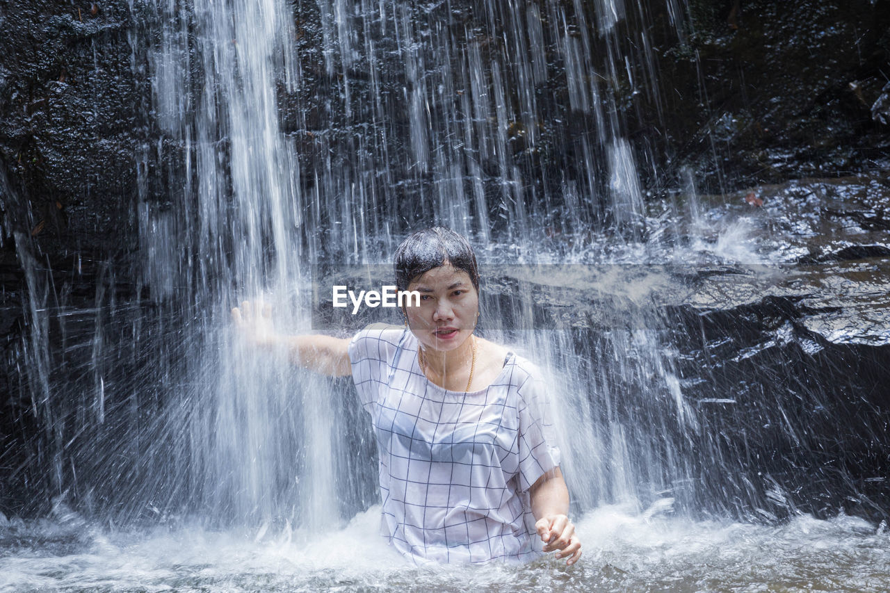 Portrait of smiling woman standing against waterfall