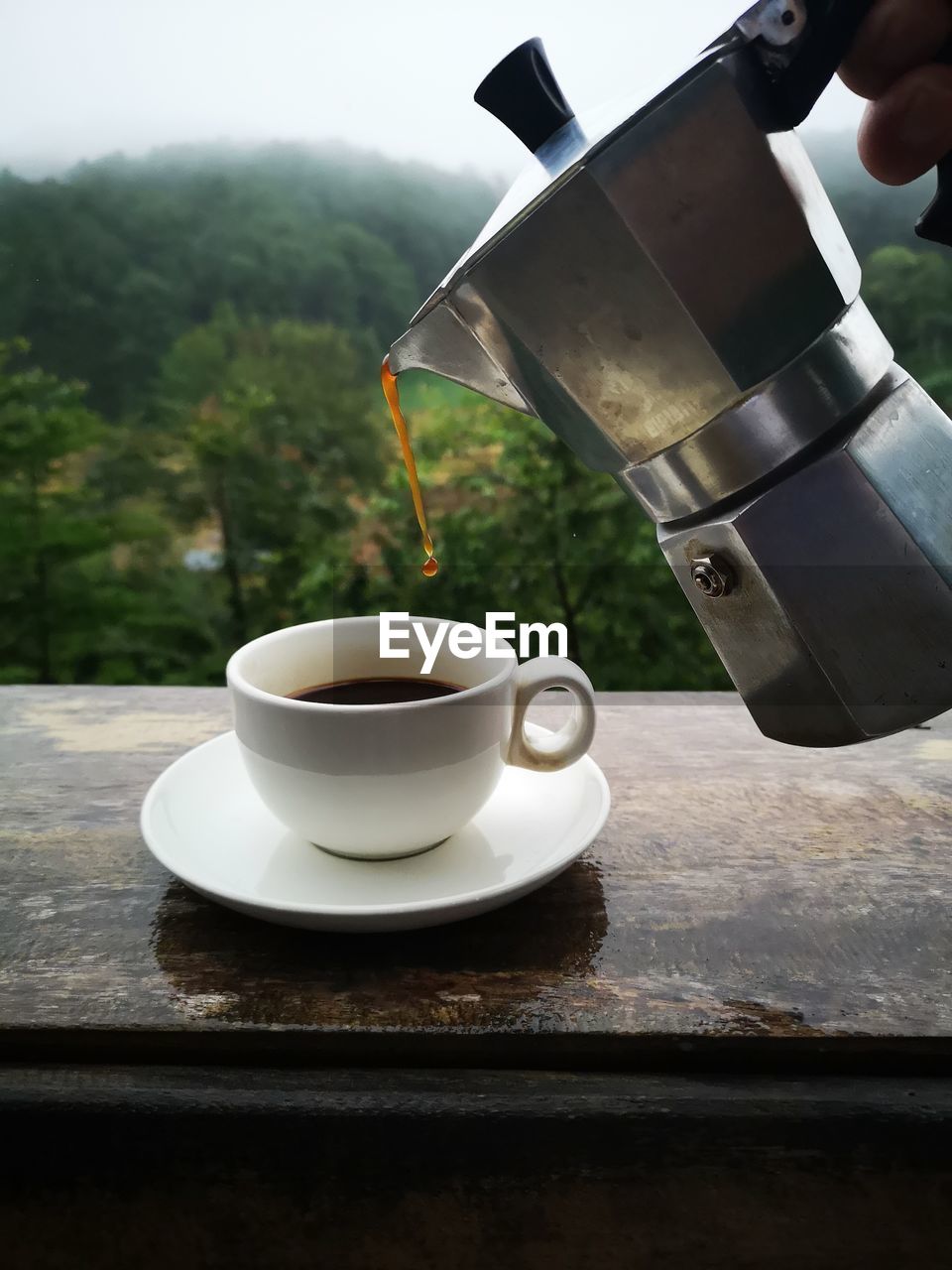 Close-up of coffee cup on table with a view of forrest behind. 