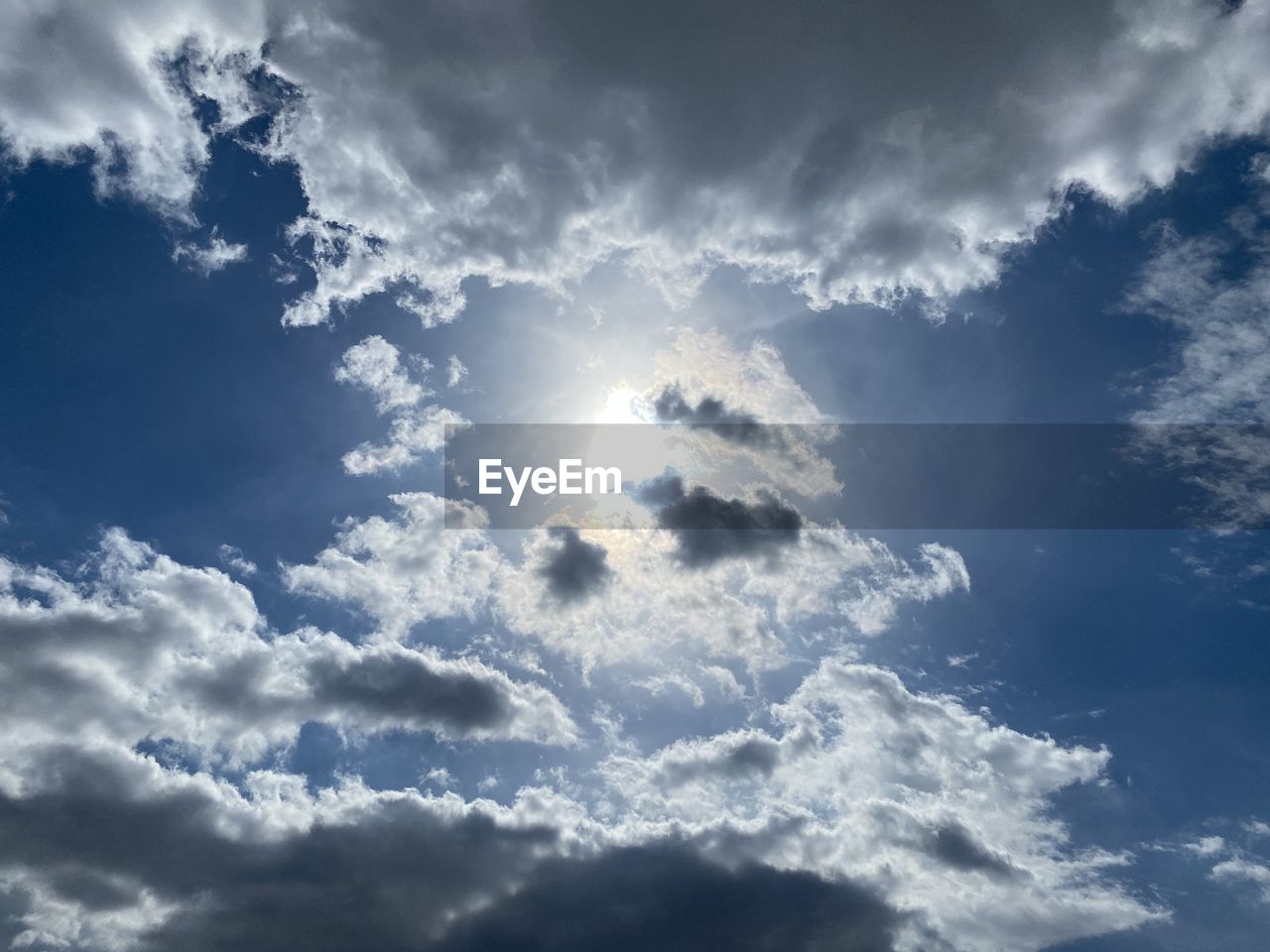 LOW ANGLE VIEW OF SUNLIGHT STREAMING THROUGH CLOUDS IN SKY