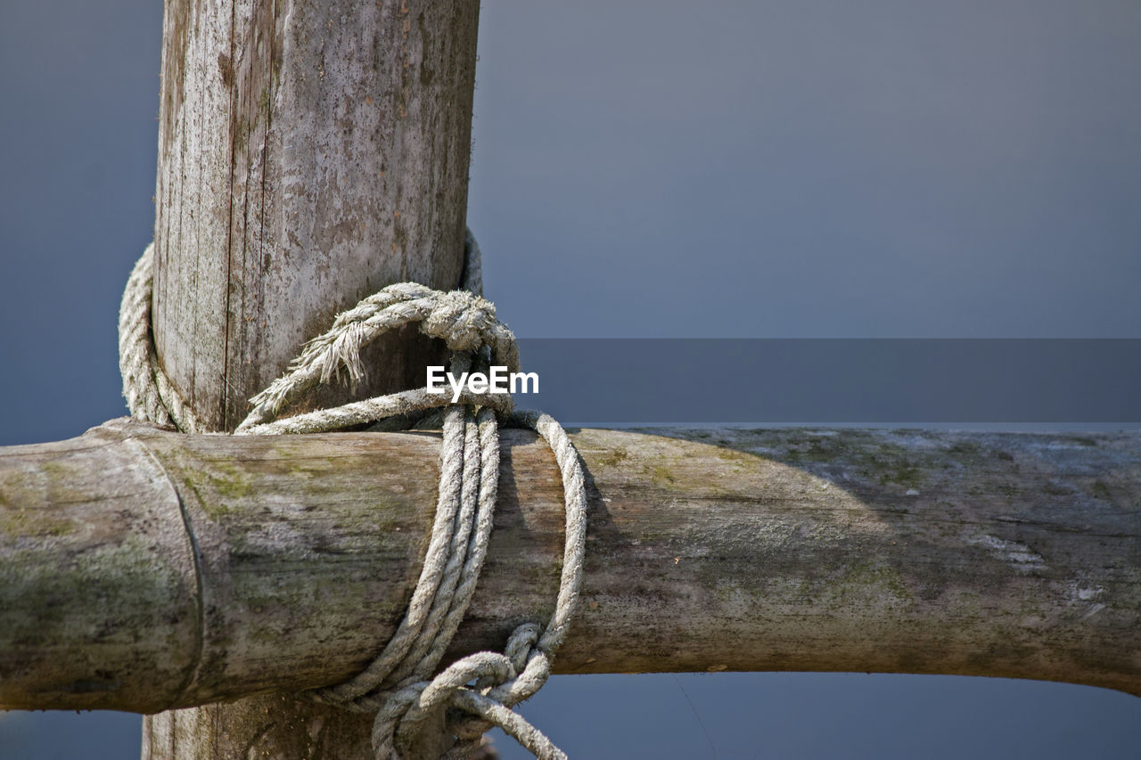 Close-up of rope tied on wooden post against sky