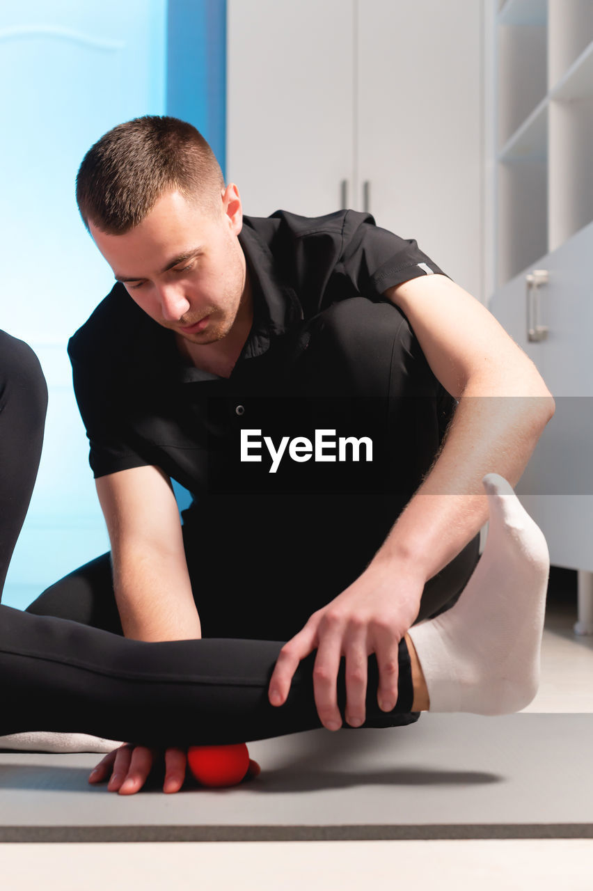 Myofascial release. a male physiotherapist puts a ball to rehabilitate the leg muscles of a client