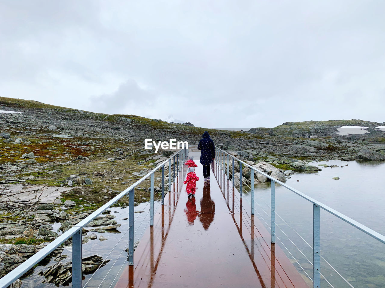 Rear view of people walking on footbridge at sea against sky