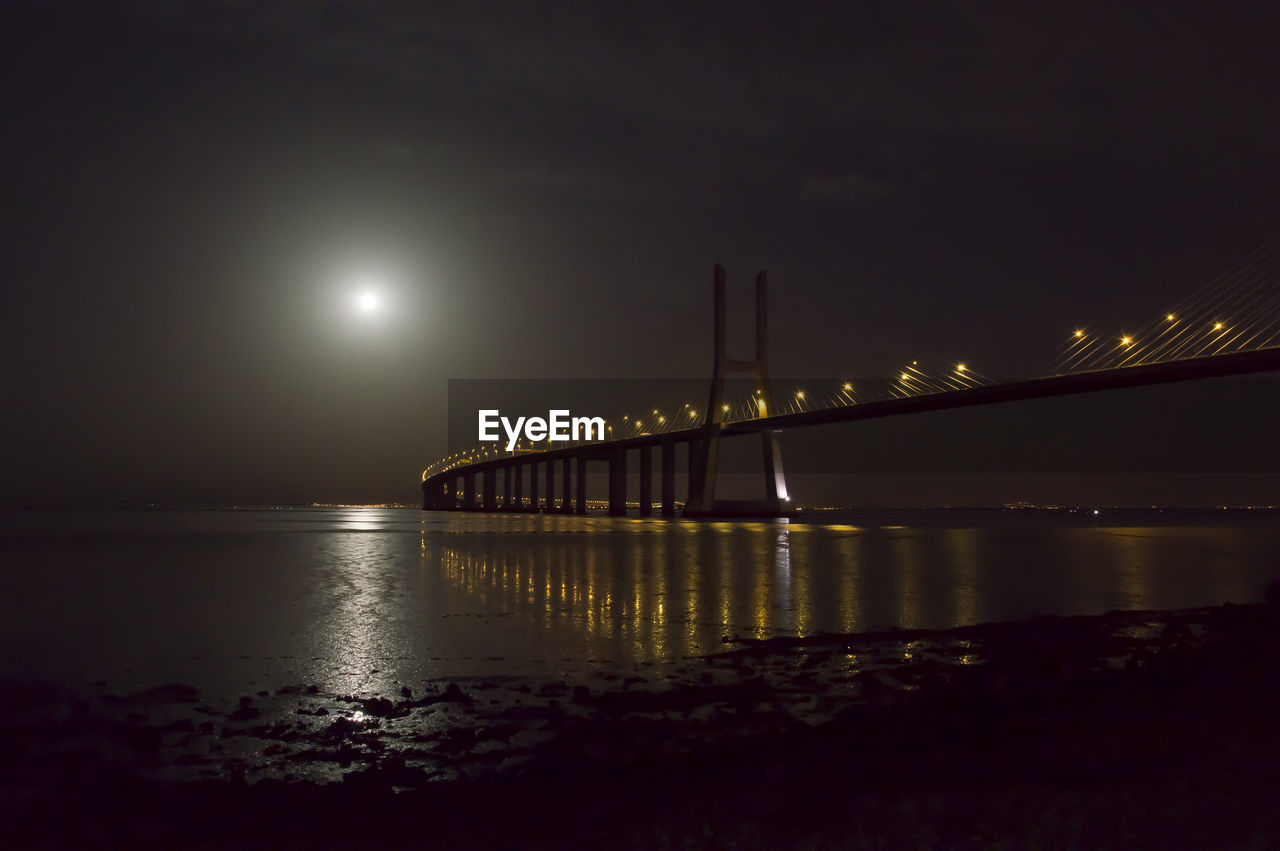 Illuminated bridge over river against sky at night