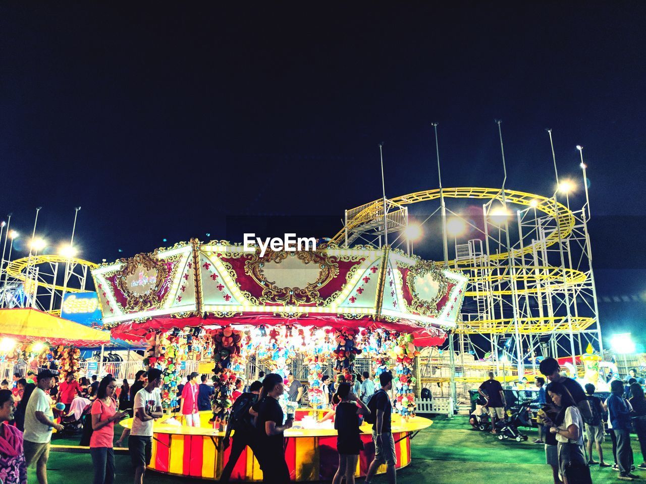 PEOPLE AT ILLUMINATED AMUSEMENT PARK AGAINST SKY AT NIGHT